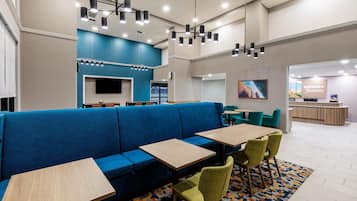 A modern hotel lobby with a blue sofa, wooden tables, green chairs, and a reception desk.