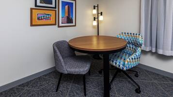 A conference room with a round table, two chairs, framed pictures on the wall, and a floor lamp.