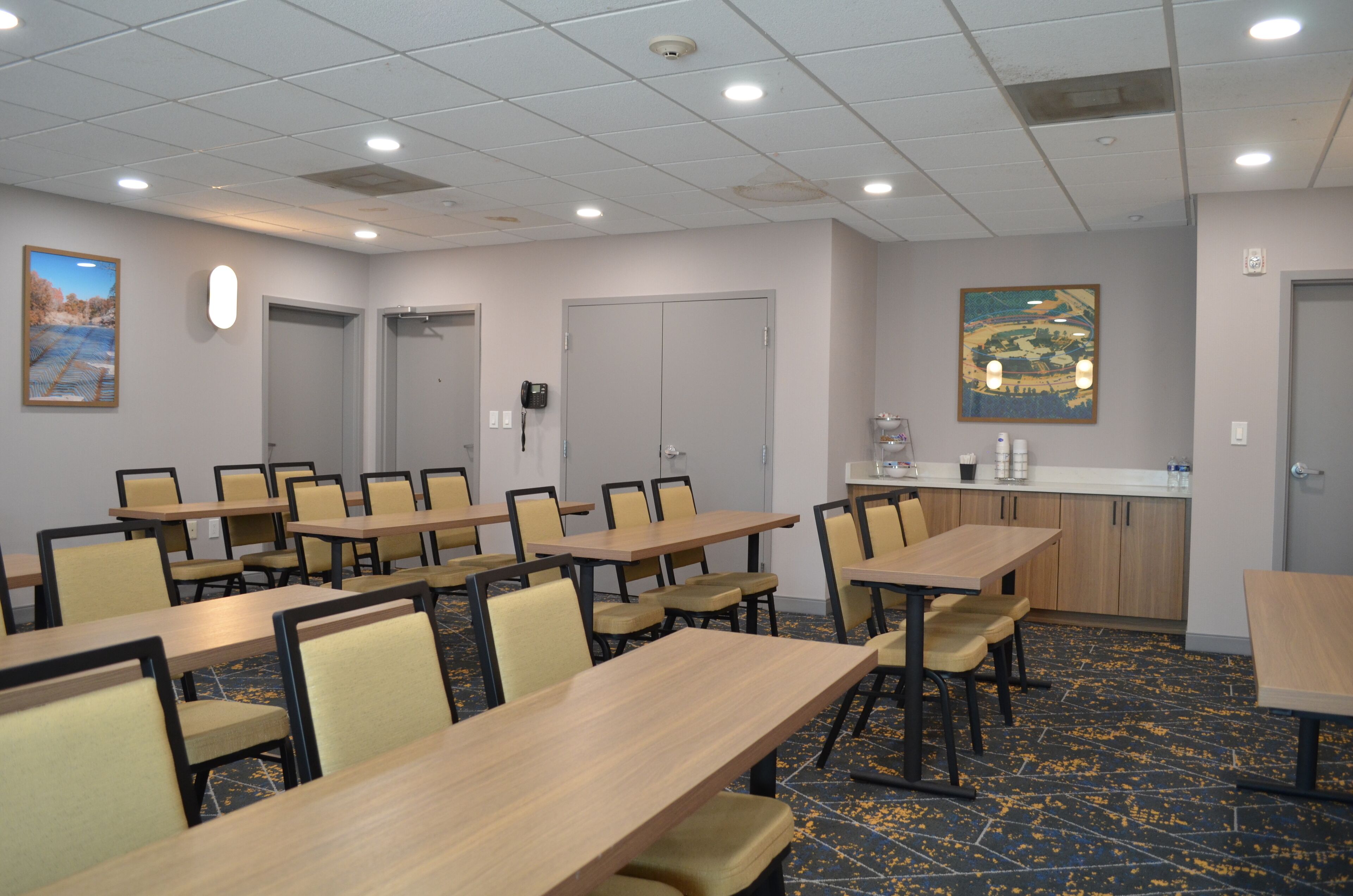 Une salle de conférence équipée de plusieurs tables et chaises, d’un coin cuisine et ornée d’un tableau.