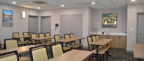 Une salle de conférence équipée de plusieurs tables et chaises, d’un coin cuisine et ornée d’un tableau.