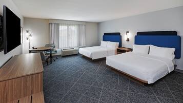 Une chambre d’hôtel avec deux lits, un bureau, une chaise, un téléviseur à écran plat et une fenêtre avec des rideaux.