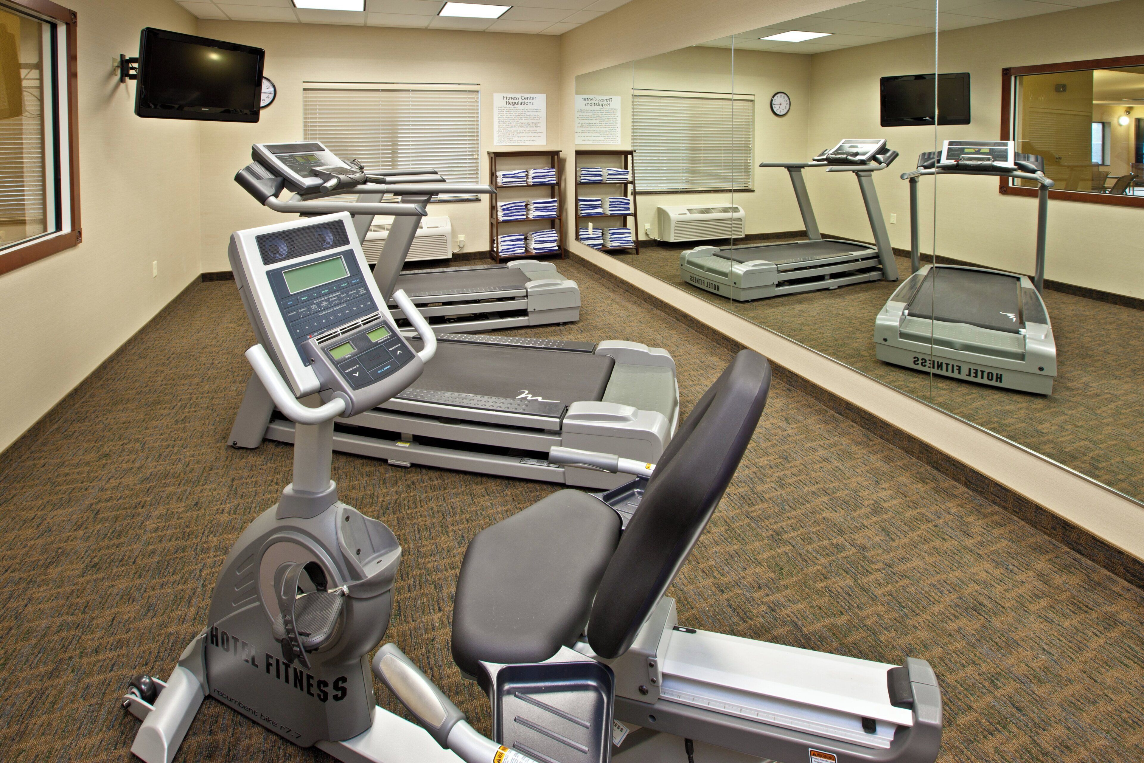 A hotel fitness center with treadmills, an elliptical, and a mirrored wall.