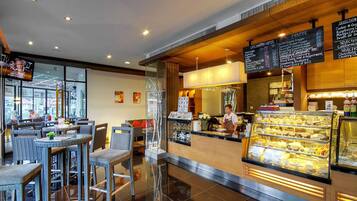 Una cafetería con mostrador, pizarras con la carta y una vitrina de pasteles.