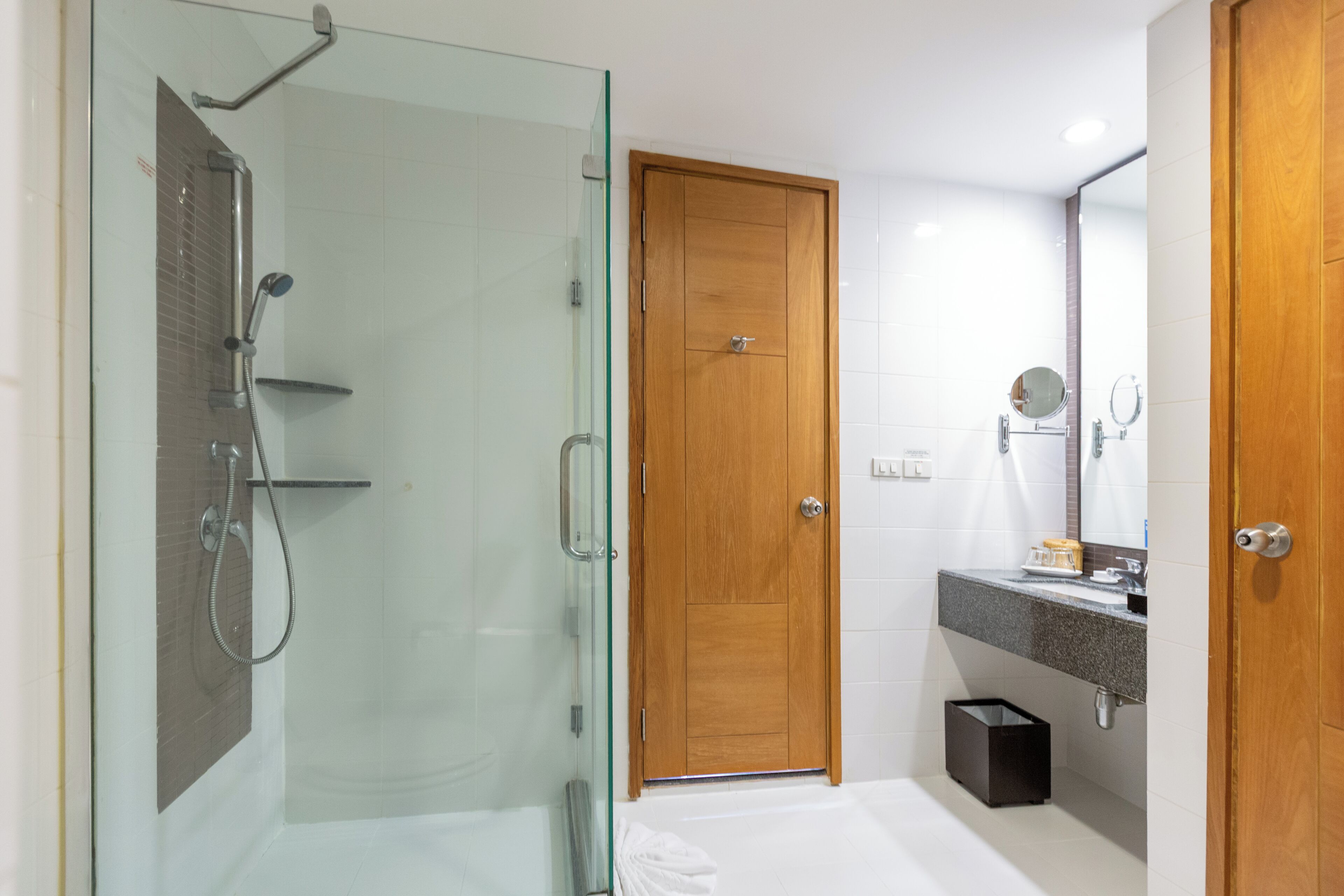 A modern bathroom with a glass shower enclosure, a wooden door, a vanity with a mirror, and a bathtub.