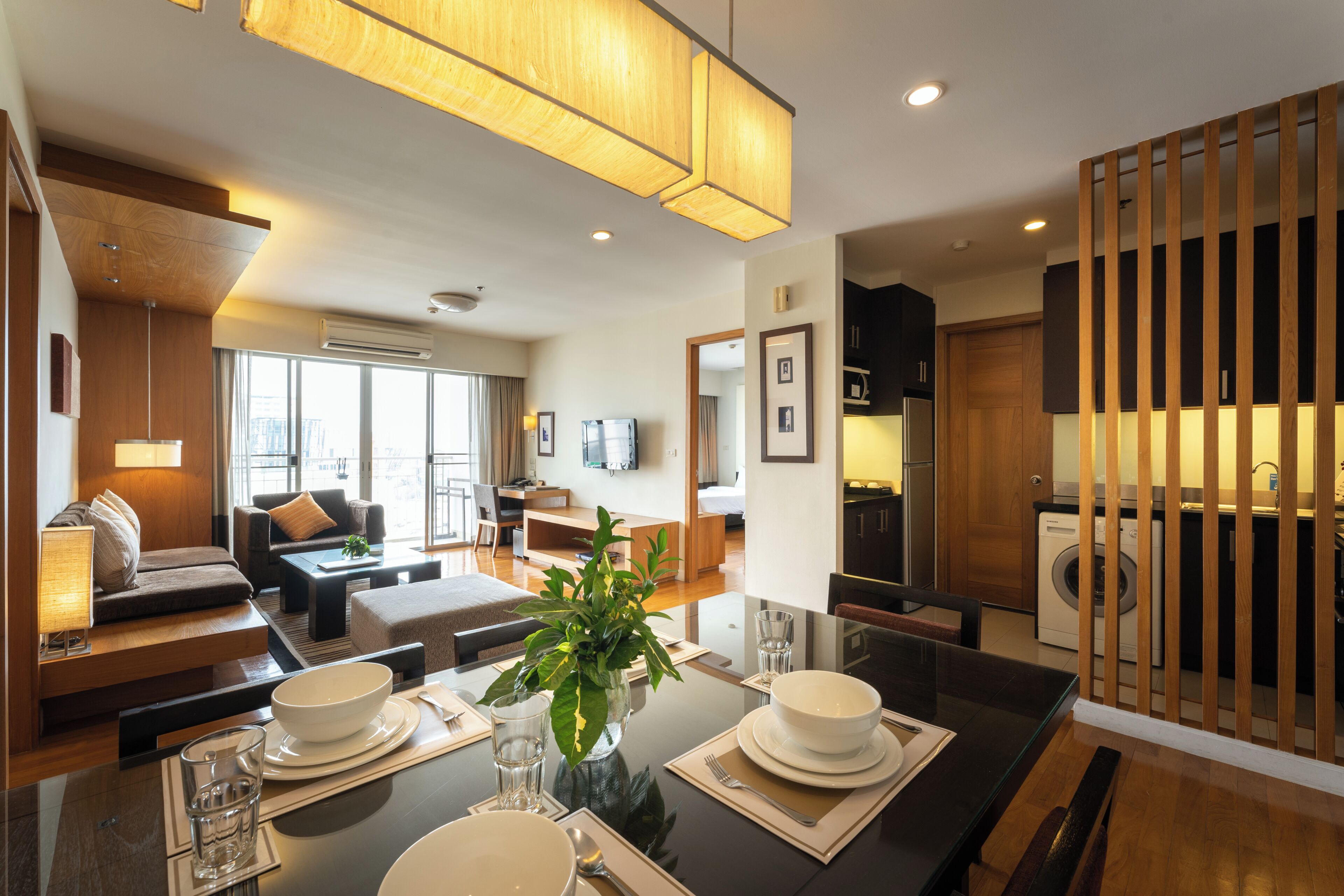 A modern hotel room with a dining area, a sofa, a TV, and a kitchen area.