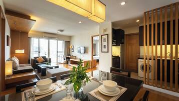 A modern hotel room with a dining area, a sofa, a TV, and a kitchen area.