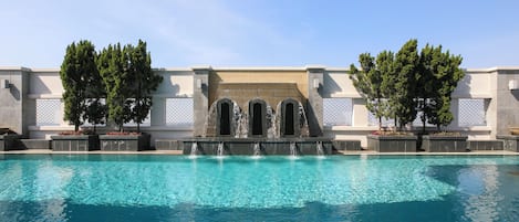 A swimming pool with a waterfall feature and trees.