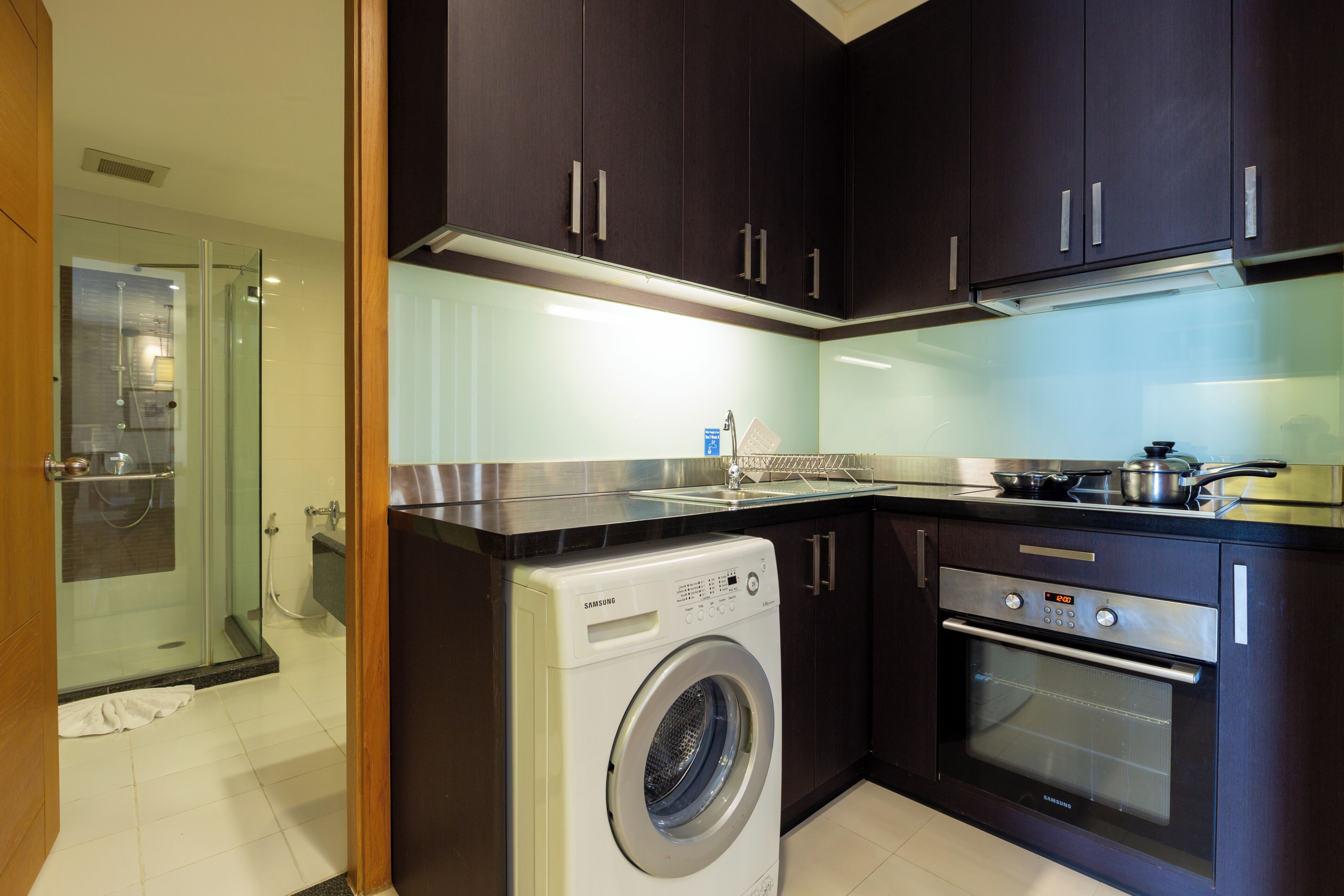 A modern kitchen with dark cabinets, a stainless steel washing machine, and an oven.