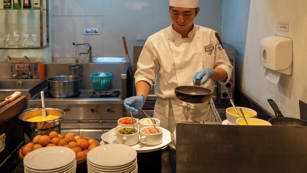 Un chef dans une cuisine professionnelle, entouré de divers ustensiles de cuisine et d’ingrédients.