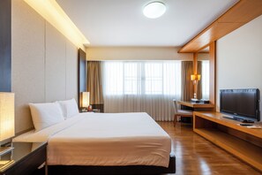 Hotelkamer met groot bed, bureau met televisie, stoel en raam met gordijnen.