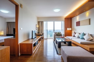 Habitación de hotel moderna con un escritorio de madera, un sofá, un televisor y un balcón con vistas.