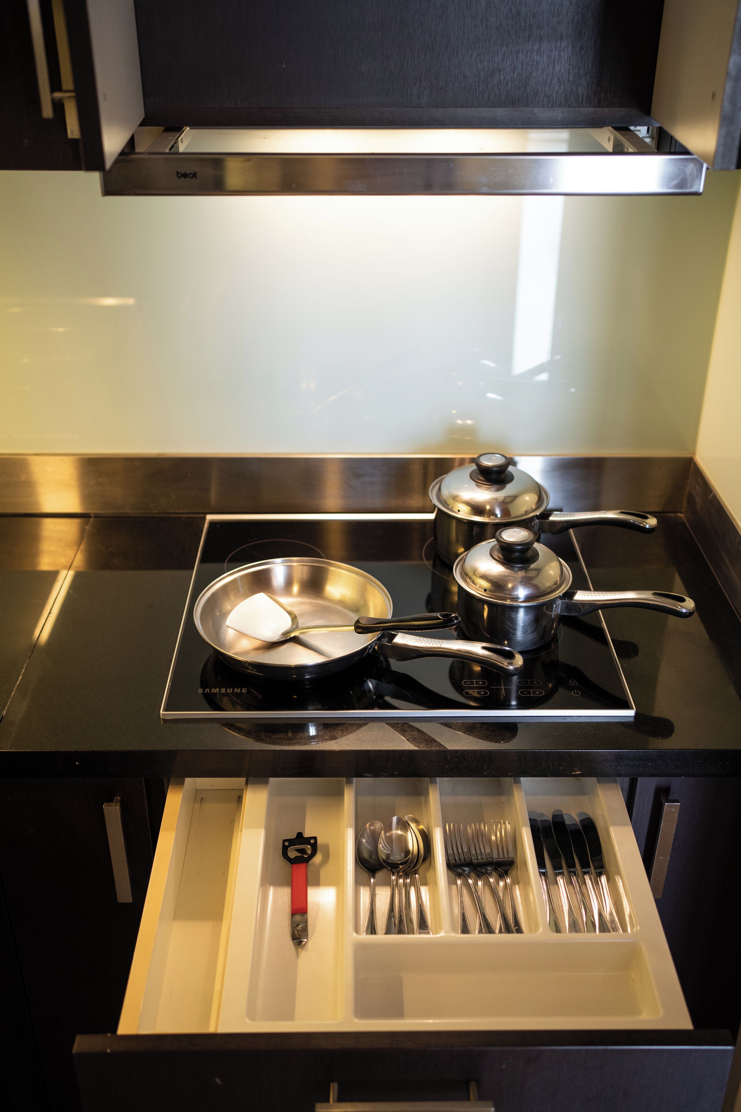 A kitchen with a stove, pots, a frying pan, and a drawer with utensils.