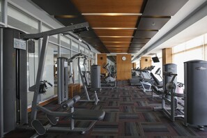Ein Fitnessraum mit unterschiedlichen Trainingsgeräten, einem gemusterten Teppich und großen Fenstern für natürliches Licht.