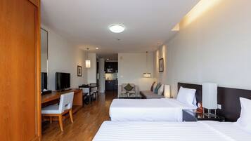 A hotel room with two beds, a desk with a chair, a television, and a kitchenette in the background.