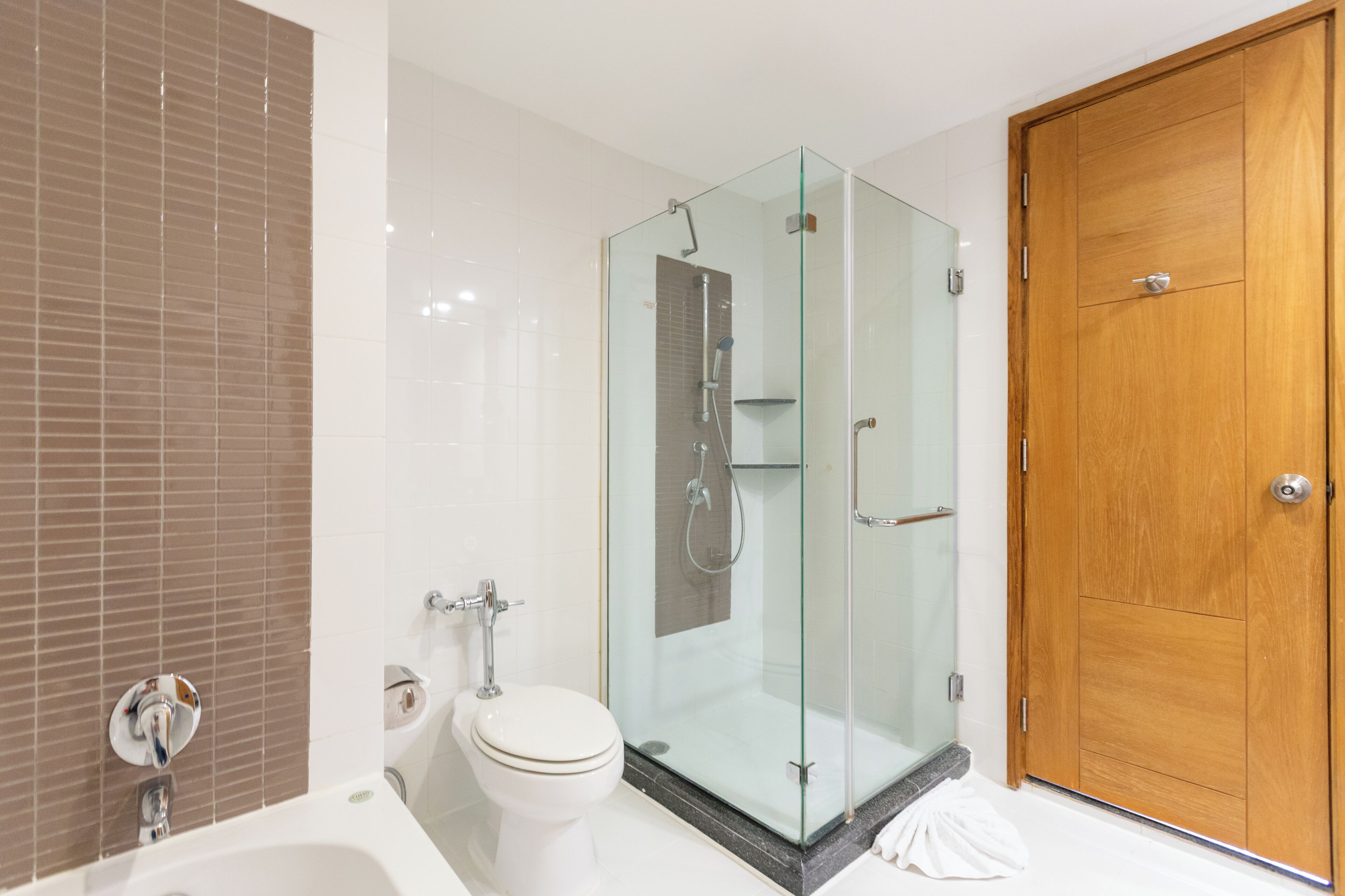 A bathroom with a glass-enclosed shower, a white toilet, and a wooden door.
