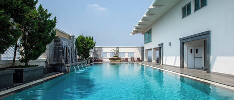 A swimming pool with a waterfall feature, surrounded by trees and a building with a modern design.