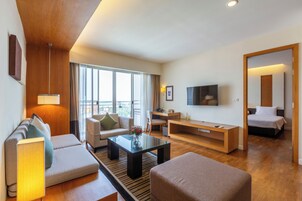 Una habitación de hotel moderna con sofá, sillón, una pequeña mesa de centro, televisor y cama.