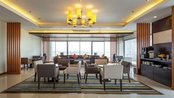 A hotel lobby with a dining area, a modern chandelier, and a large window providing a view.