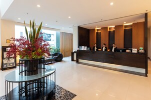 Un área de recepción con mostrador, un espacio de espera con mesa y sillas, y una planta en maceta con flores rojas.