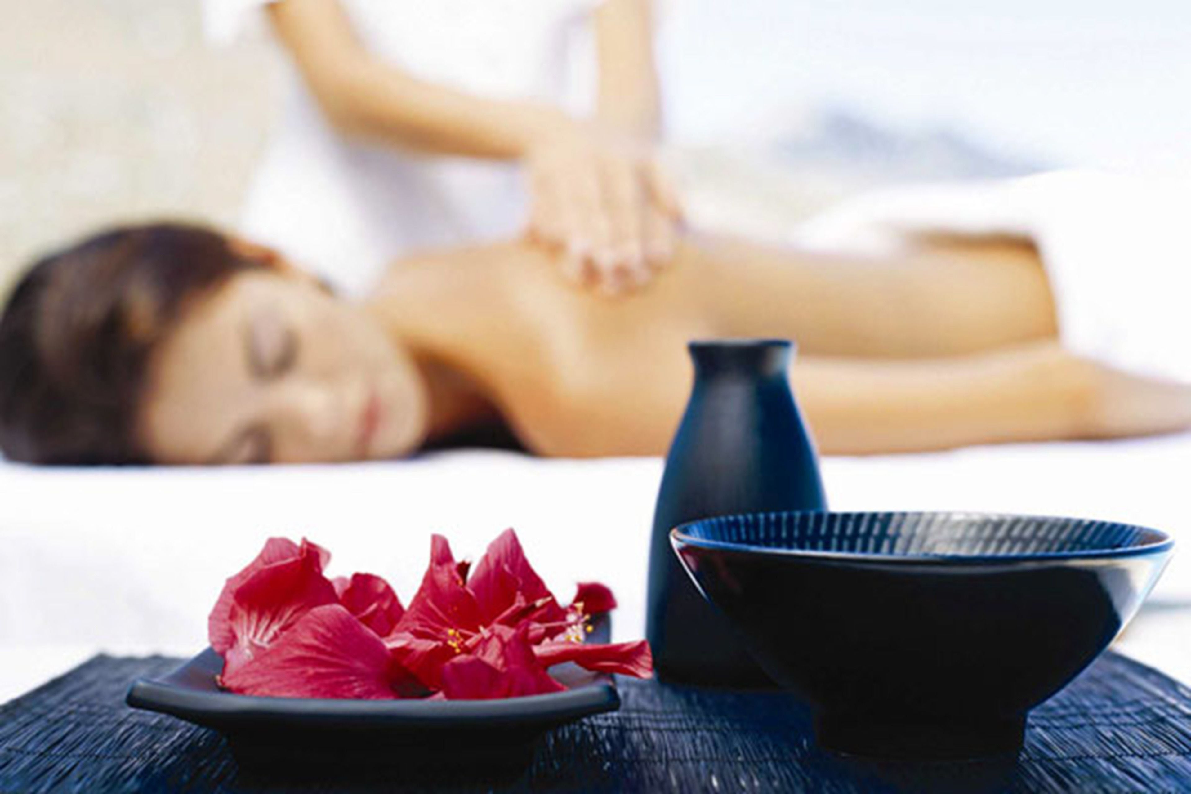 Un espacio de spa con una camilla de masaje, un recipiente y flores rojas sobre una mesa.