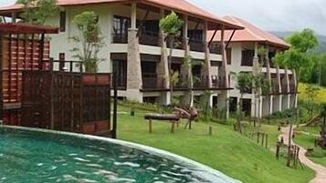 Hotel features a pool surrounded by a lawn and trees, with a pathway leading to the water.