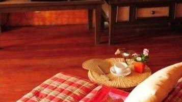 Una sala de estar acogedora con un televisor sobre un soporte de madera, un sofá cómodo con una manta roja y beige, y una mesita con una tetera y tazas.