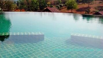 A clear pool with a tiled bottom, surrounded by trees and a hilly landscape.