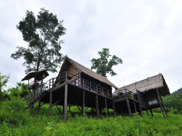 A treehouse-style building with a thatched roof, wooden deck, and a staircase leading to the upper level. - Phunacome Resort (Dan Sai)