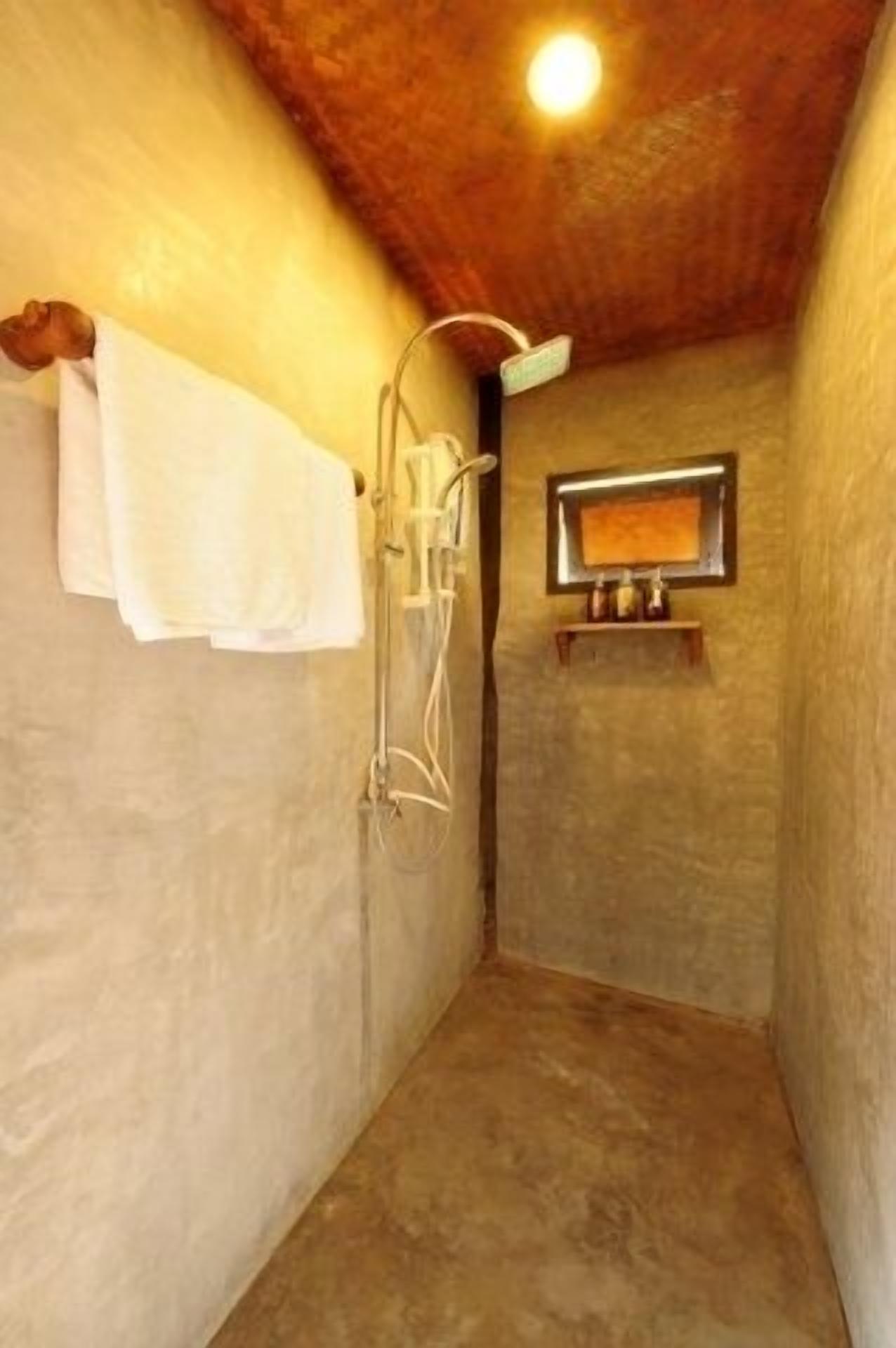 Une petite salle de bain fermée, équipée d’une douche, d’un porte-serviettes et d’une étagère où sont rangés les articles de toilette.