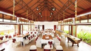 Un amplio salón con techos altos e iluminación natural gracias a grandes ventanales. Las mesas están dispuestas con manteles blancos y fajines rojos.