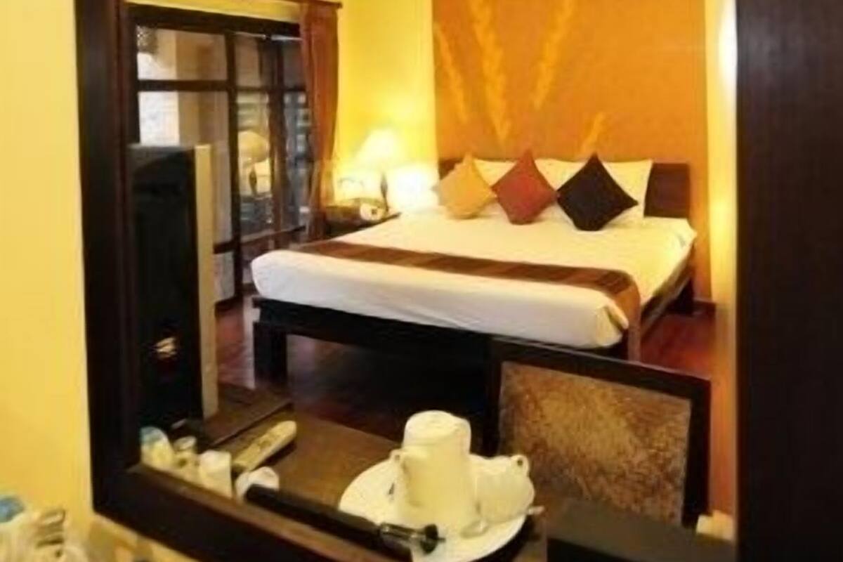 A hotel room with a bed, bedside table, and a mirror reflecting the room.