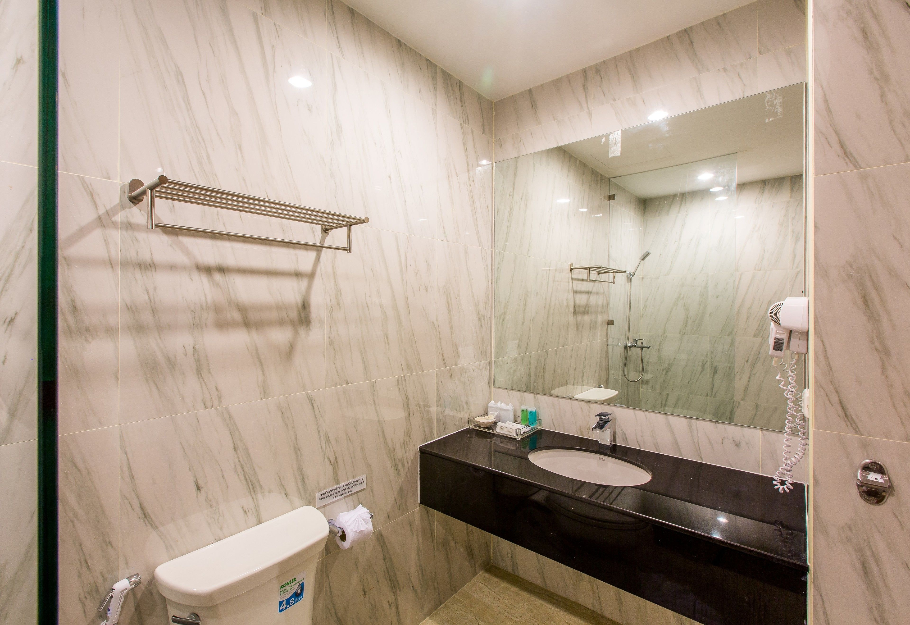A modern bathroom with a marble wall, a black sink, and a glass shower enclosure.