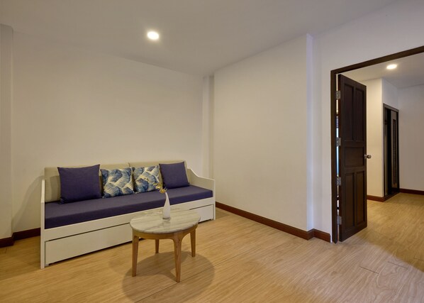 A modern living room with a sofa, a small round table, and a door leading to another room. - Nai Yang Beach Resort & Spa (Sa Khu)