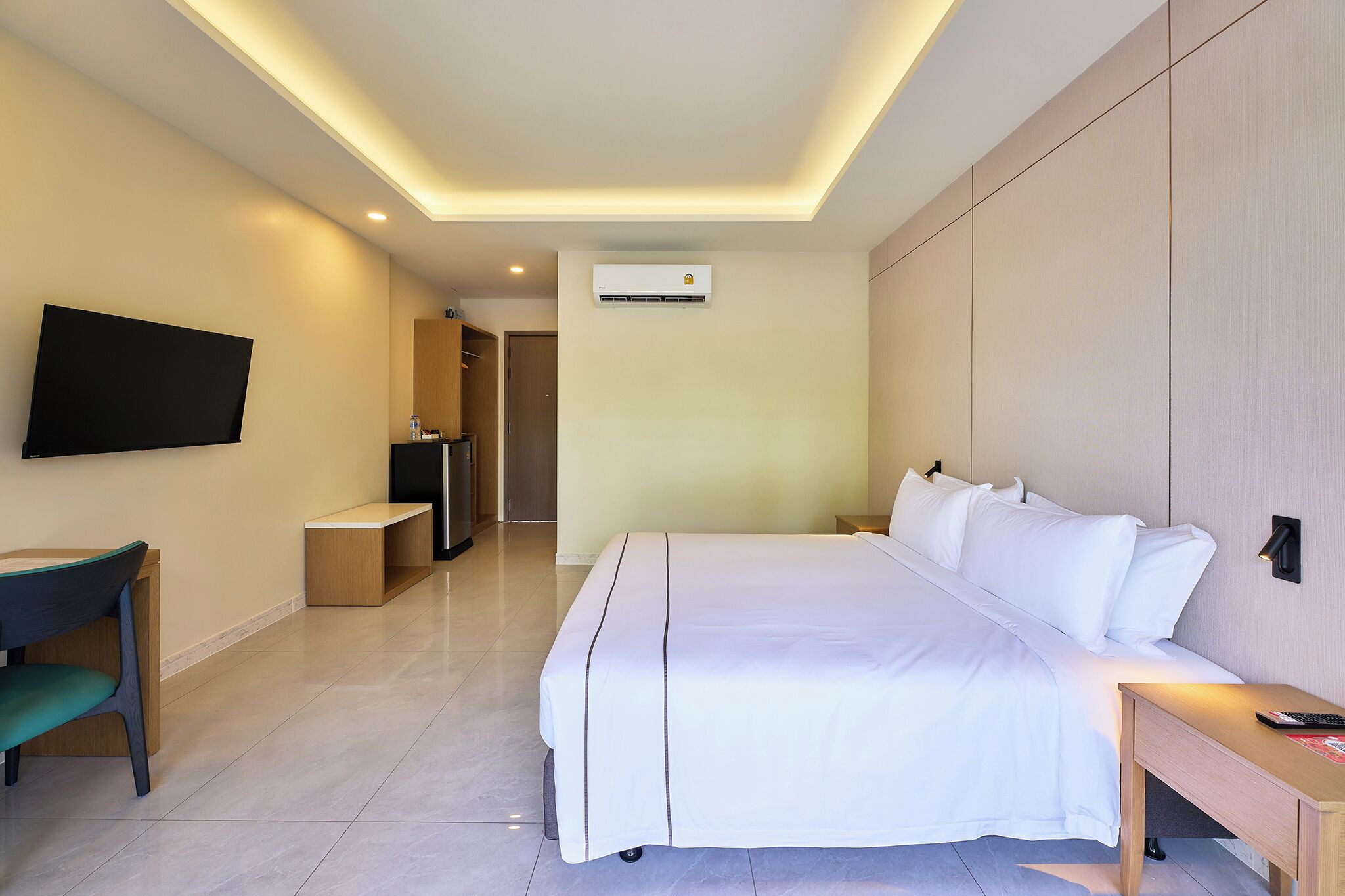 Een hotelkamer met een bed, nachtkastje, stoel, televisie en een airconditioning.