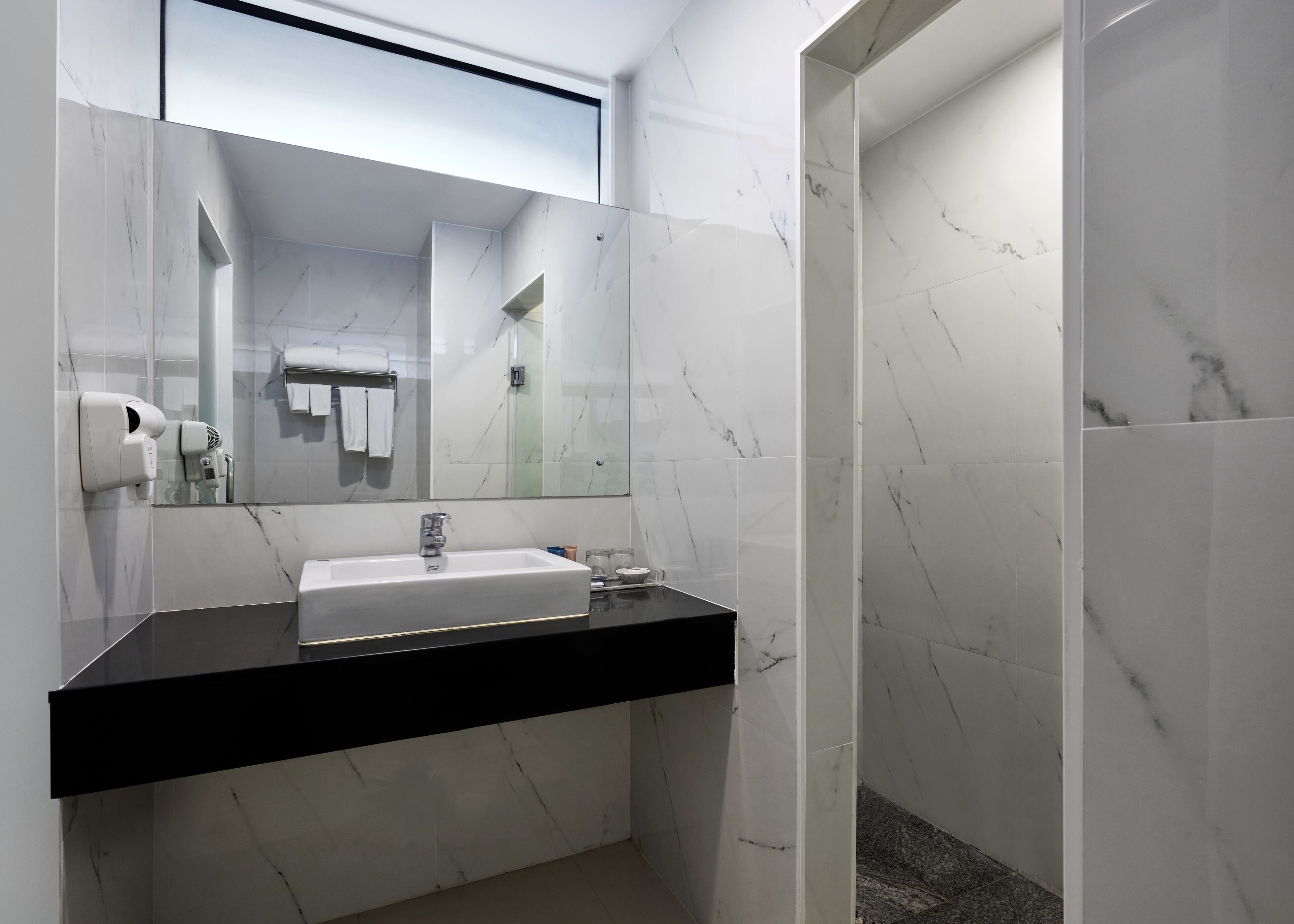 Une salle de bain moderne avec un plan de toilette noir, un lavabo blanc et des murs en marbre.