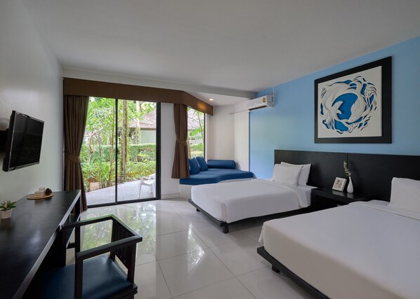 Habitación de hotel con dos camas, un escritorio, televisión y un ventanal con vistas a zonas verdes.