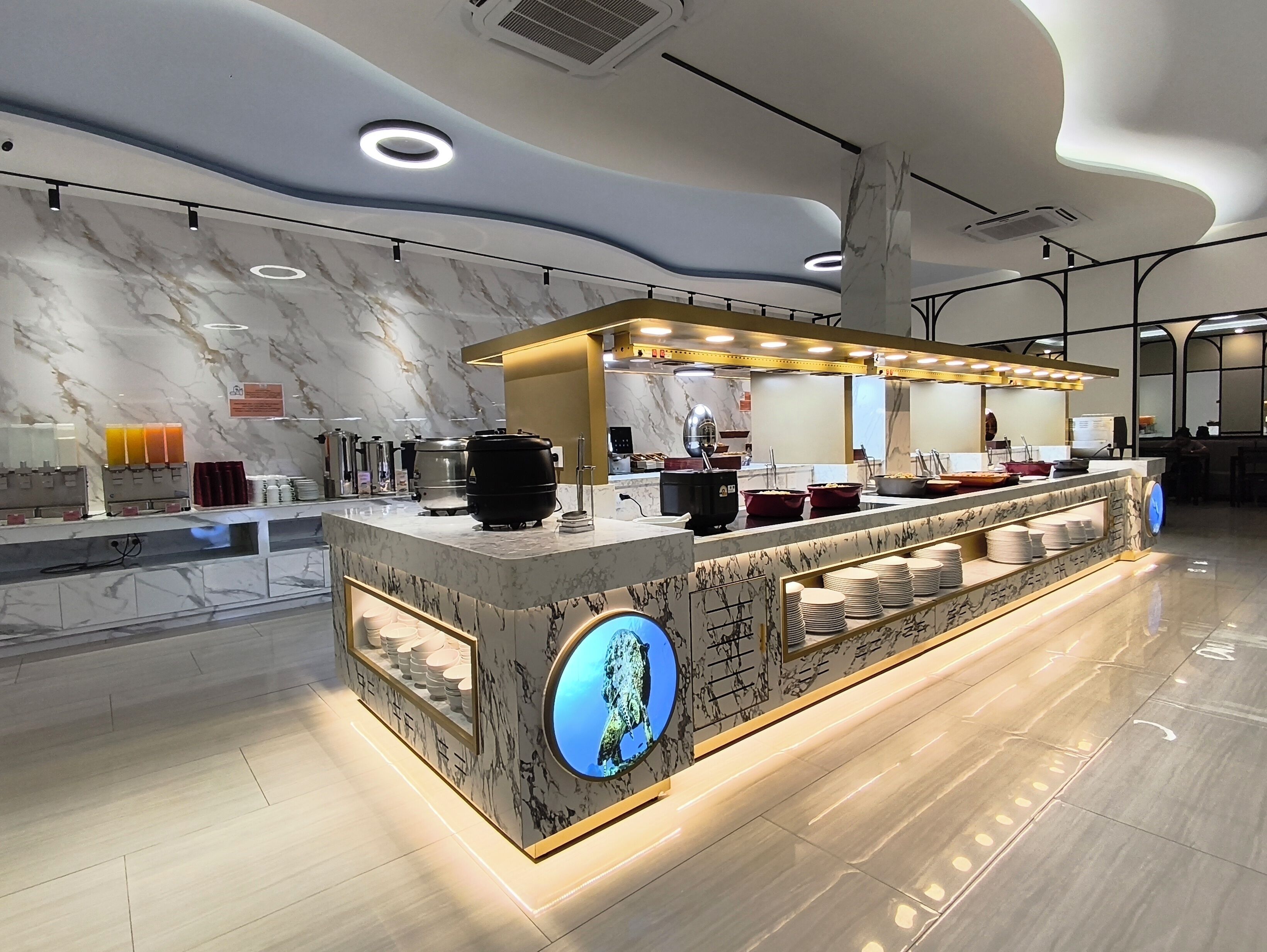 A modern, well-lit buffet area with marble countertops, a central island with a globe decoration, and a variety of food and drink dispensers.