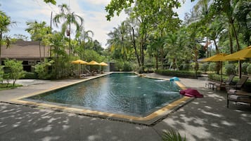 A swimming pool with lounge chairs and umbrellas, surrounded by lush greenery and palm trees.