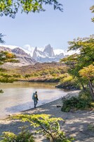 A person walking along a lakeside path with mountains in the background.
