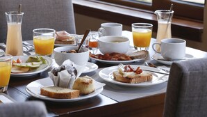 A breakfast table with various dishes and drinks, set against a window with a view of a mountainous landscape. - Los Cerros del Chalten Boutique Hotel (El Chalten)
