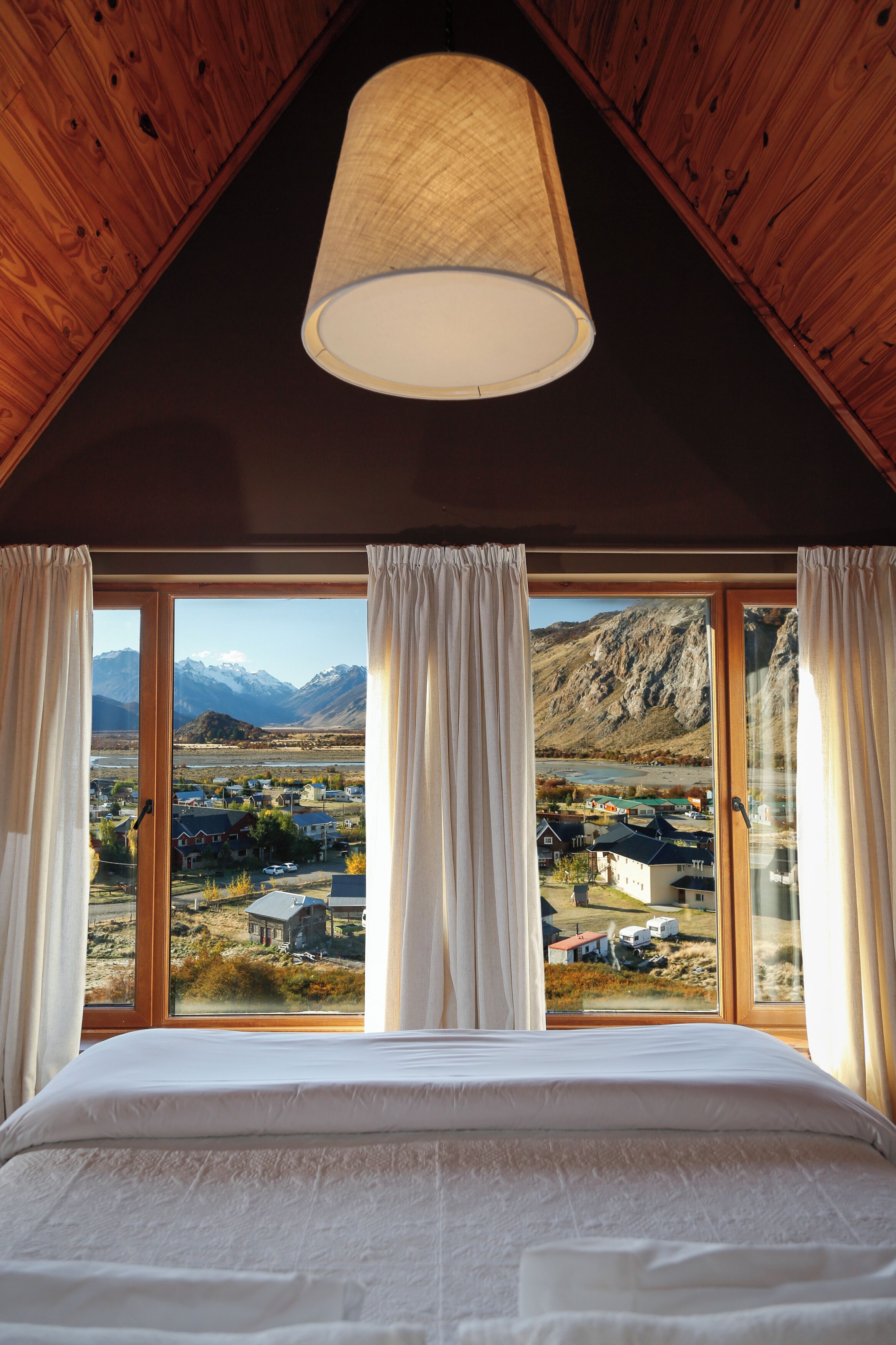 Ein Schlafzimmer mit einem großen Bett, Holzboden und Blick auf eine Stadt und Berge durch ein großes Fenster.