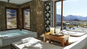 A spa room with a hot tub, two sun loungers, a wooden table with a tray, and a stone wall.
