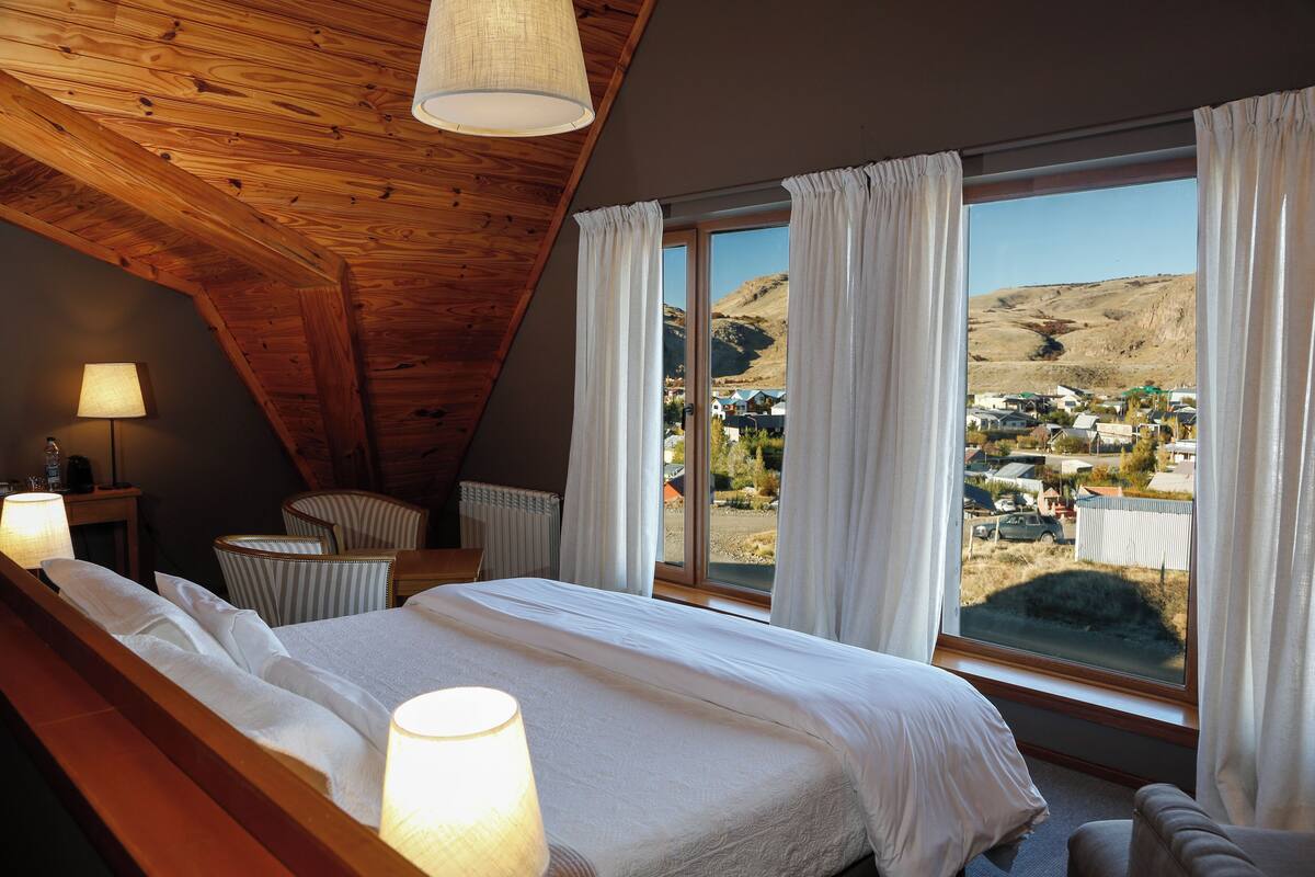 A bedroom with a large window, a bed, a chair, and a lamp.
