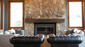 A living room with a stone fireplace, leather ottomans, and large windows. - Los Cerros del Chalten Boutique Hotel (El Chalten)