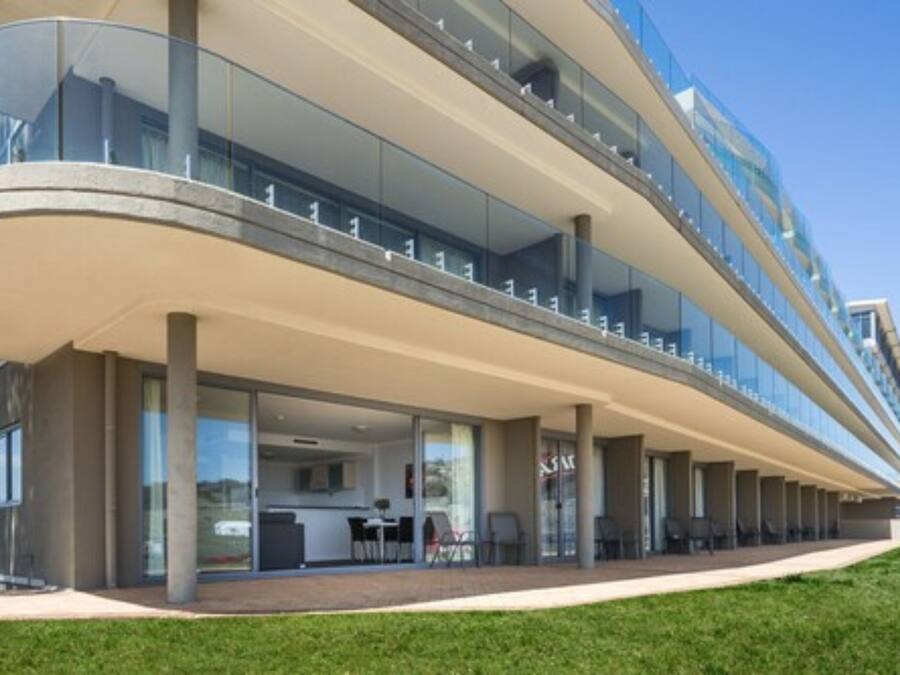 A modern hotel with a curved glass facade, outdoor seating area, and a covered walkway.