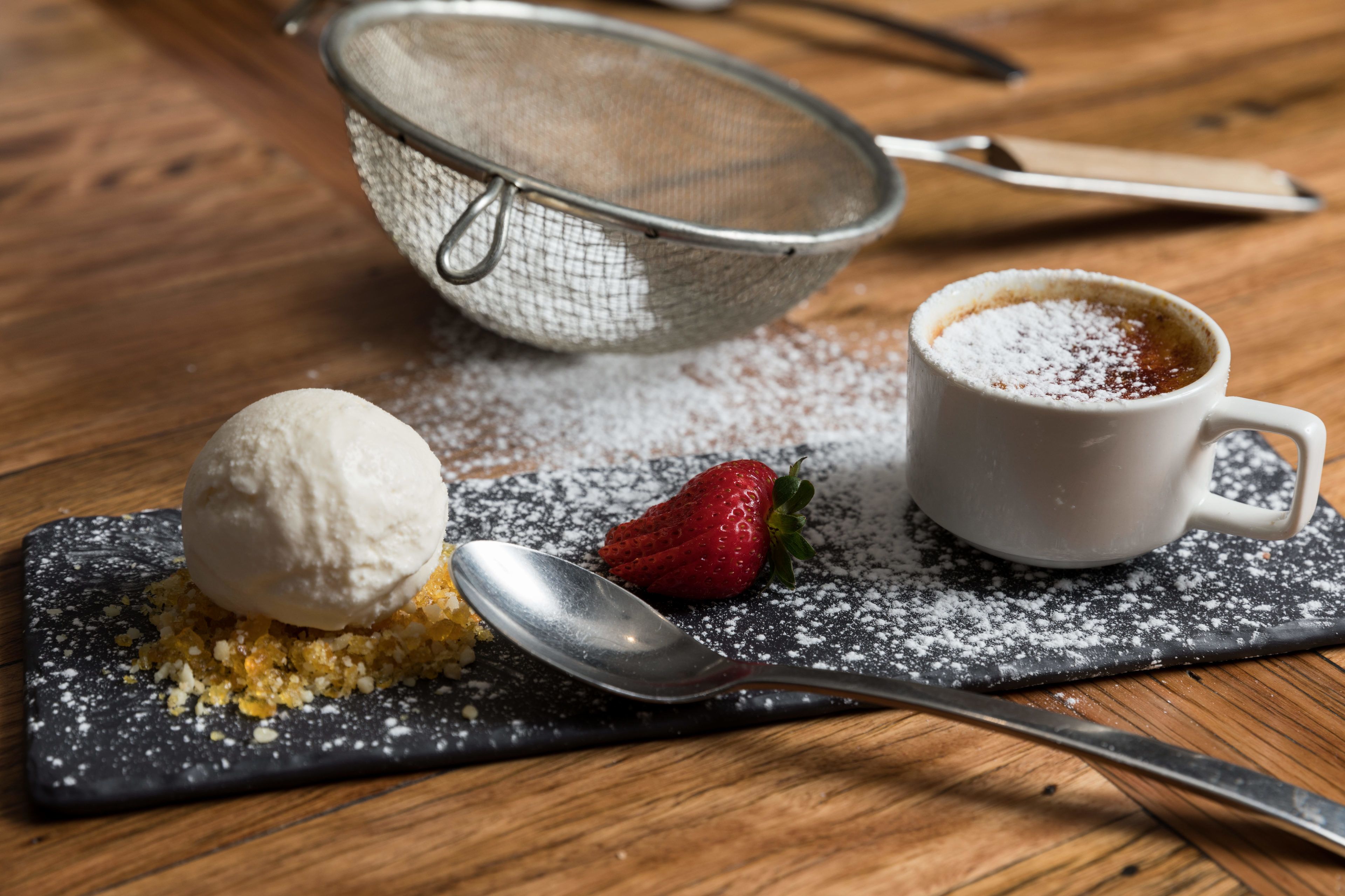 Une assiette à dessert avec une boule de glace, une fraise et une tasse de café, le tout posé sur une table en bois.