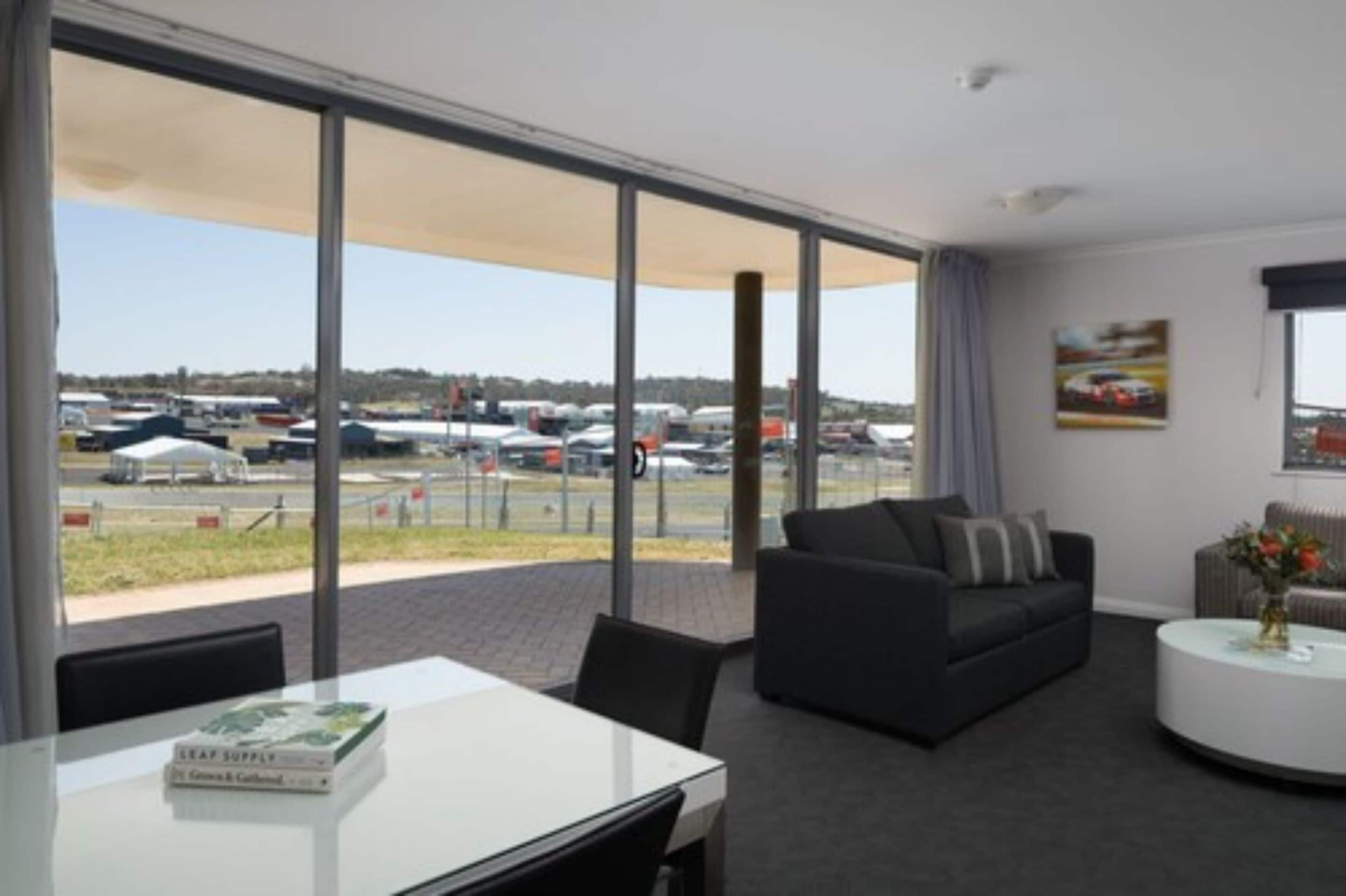 Habitación de hotel moderna con un amplio ventanal que ofrece vistas a coches estacionados y un paisaje distante.