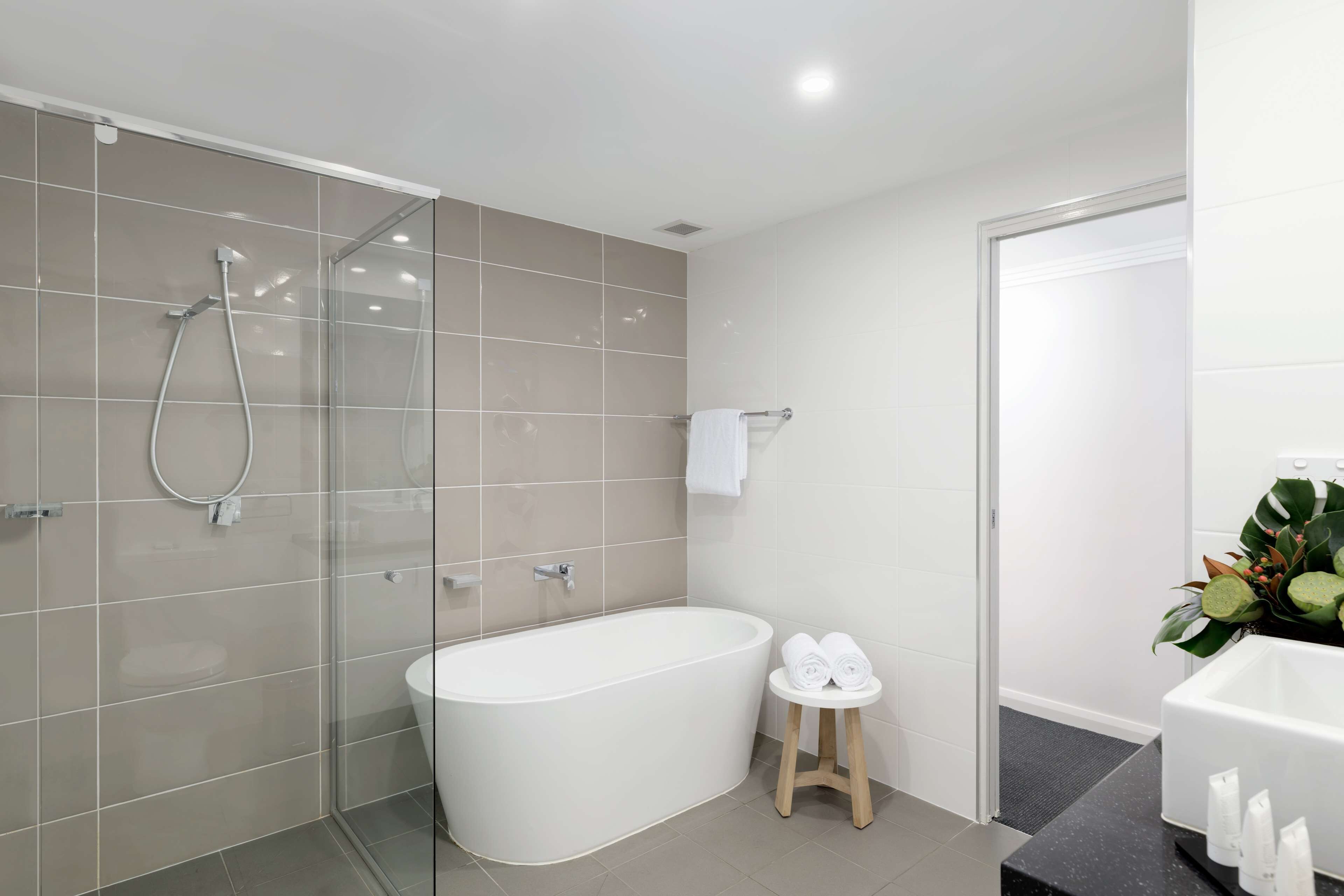 Un baño moderno con ducha acristalada, bañera independiente y un taburete con toallas.