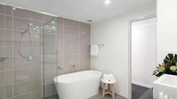 Un baño moderno con ducha acristalada, bañera independiente y un taburete con toallas.