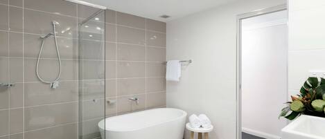 Un baño moderno con ducha acristalada, bañera independiente y un taburete con toallas.